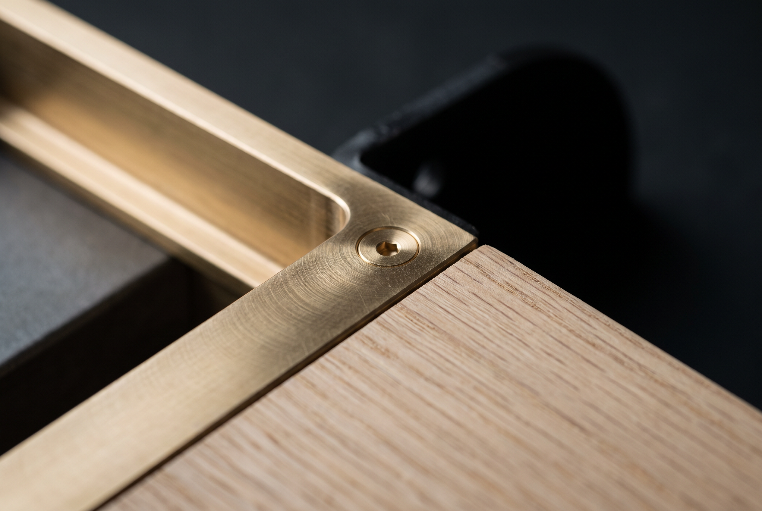 Close detail of a brushed brass inset pull meeting an oak drawer front, fixed with a countersunk brass screw